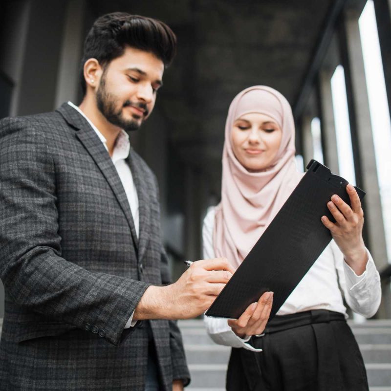 woman-in-hijab-holding-clipboard-while-man-signing-XZYLMHE.jpg